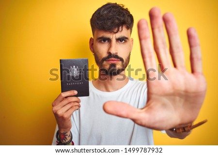 Young man with tattoo wearing Australia Australian passport over isolated yellow background with open hand doing stop sign with serious and confident expression, defense gesture