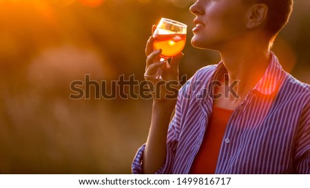 Happy brunette woman holding orange cocktail over sunset sky in orange colors