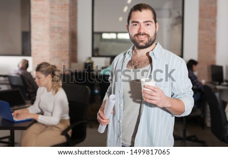 Portrait of cheerful male entrepreneur during daily work in modern office with coworkers 