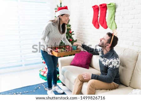 Happy woman serving snacks to man sitting on sofa at home during Christmas season