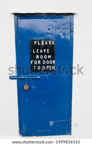 Blue metal door on a building with a sign "Please leave room for door to open"