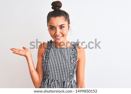 Beautiful woman with bun wearing casual dresss standing over isolated white background smiling cheerful presenting and pointing with palm of hand looking at the camera.