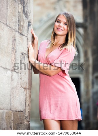 Positive young woman standing near old stone wall while strolling around city