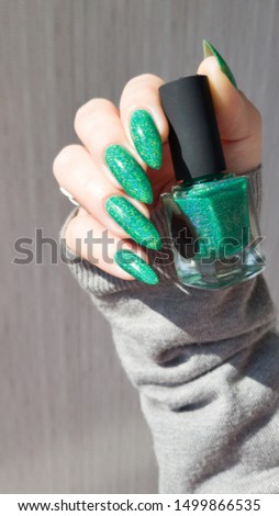 Female hand with long nails and a bottle of bright neon green nail polish