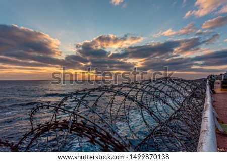 Balker in a pirate area of Africa. The photo shows a barbed wire against a sunset. Barbed wire on merchant ships is installed to protect against pirate attacks. Royalty-Free Stock Photo #1499870138