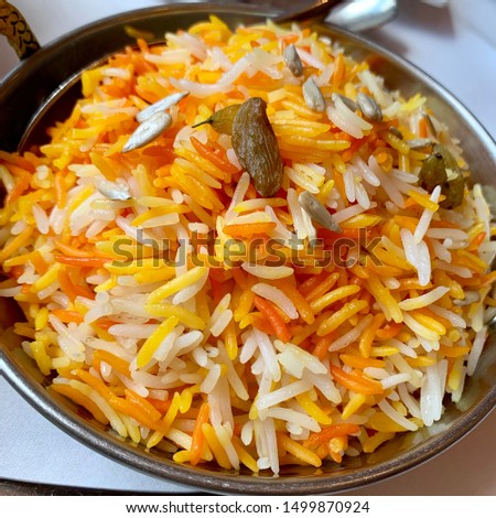 Indian Saffron Rice (Kesar Pulao). Made with Basmati Rice , flavored & coloured with saffron (kesar) and turmeric powder, garnish with raisins and sunflower seeds. Served in brass pan. Selective focus Royalty-Free Stock Photo #1499870924