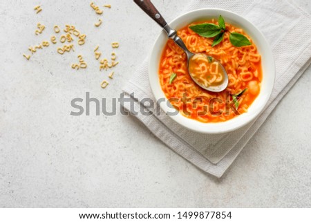 Alphabet Tomato Soup. Vegetable soup with alphabet pasta on white background, copy space, top view. Minestrone soup for kids. Royalty-Free Stock Photo #1499877854