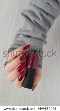 Female hand with long nails and a bottle with red bordo nail polish