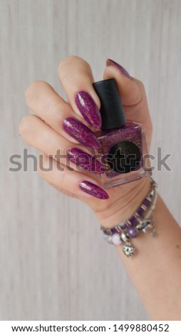 Female hand with long nails and a bottle with red bordo nail polish