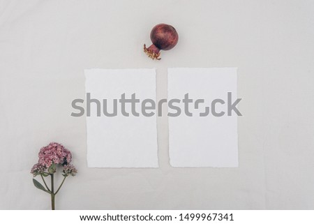 Minimalistic wedding composition with cards mock up, flowers, pomegranate on white background. Flat lay, top view stylish art concept.