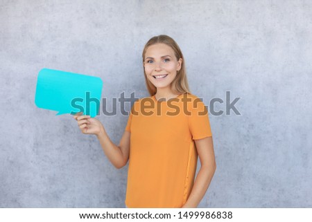 Happy beautiful young blonde woman standing isolated over gray background, holding empty speech bubble