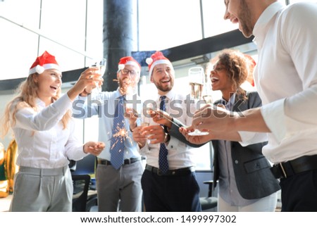 Young business partners are lighting bengal lights and drinking champagne in a modern office. Merry Christmas and Happy New Year.