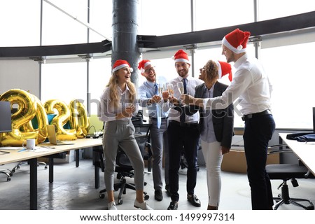 Business people are celebrating holiday in modern office drinking champagne and having fun in coworking. Merry Christmas and Happy New Year 2020.