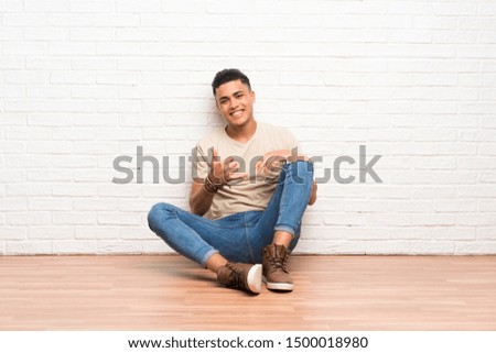 Young man sitting on the floor making phone gesture