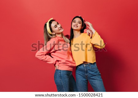 Beautiful Asian girls in sweaters and jeans posing on red background