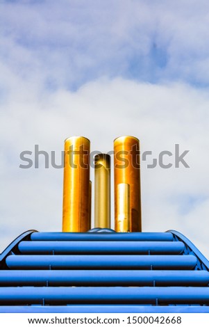 Simple graphic front view of ship exhaust pipes and blue cowling against blue sky with clouds.