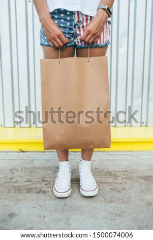 Girl is holding blank shopping brown kraft bag in hand for branding. Empty blank paper bag with handles without inscriptions and logos. Delivery food.