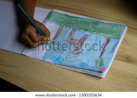 The child's hands are painted with colored pencils in a paper ona a wooden background