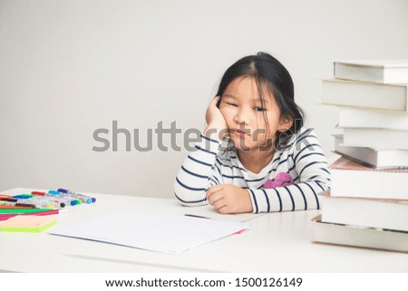 A girl studying at an elementary school level is tired of studying, with books full of her desk, she doesn't feel fun. Educational concepts for young children