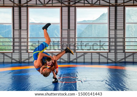 A  wrestler boy in a sports tights wrestles with an adult male wrestler on a wrestling carpet in the gym. The concept of child power and martial arts training. Teaching children Greco-Roman wrestling
