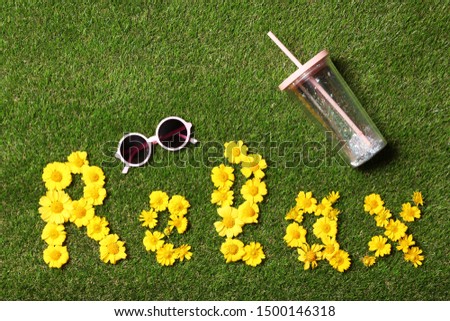 Flat lay composition with word RELAX of yellow flowers on green grass