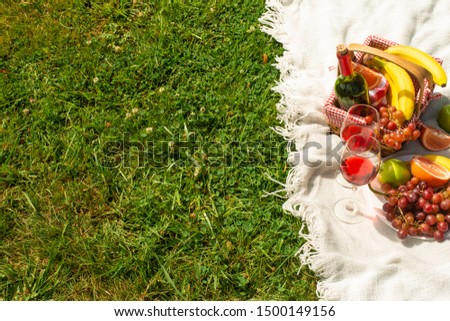 Flat lay Picnic on a green lawn, with a plaid fruit and picnic basket and a bottle of wine and glasses with red wine, with space. Summer mood and outdoor recreation