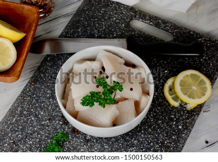 Pieced of wild caught halibut on a cutting board, seafood day, making seafood, white raw fish in a bowl  with a knife and sliced lemon