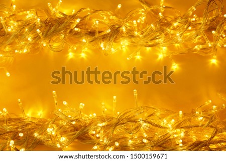 Glowing Christmas lights on yellow background, top view. Space for text