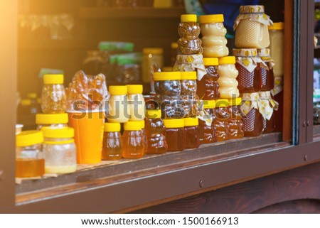 Small jars of golden and white honey in the form of bears stand on a wooden counter in the market during the trade. Health and organic foods with sun shining. Beekeeping and apiaries.