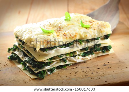 Tasty healthy portion of vegetarian spinach lasagne with alternating layers of pasta and fresh green spinach leaves with cheese on a wooden board