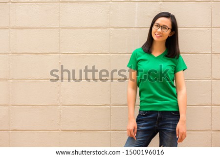 young attractive girl wearing a green t shirt standing on brick wall background , copy space.
