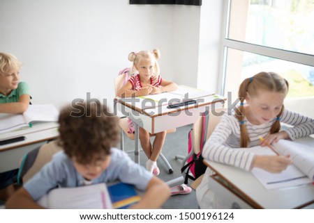 Cute blonde girl. Cute blonde-haired girl sitting at the desk near window and listening to teacher