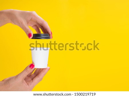 Female hands opening a small paper coffee cup isolated on a yellow background. Opened white espresso cup mockup with copy space for banner or logo