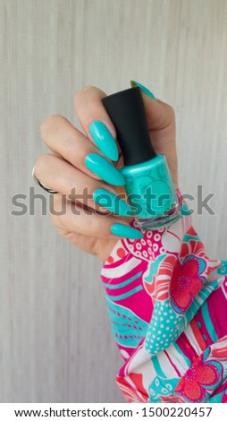 Female hand with long nails and a bottle of bright neon nail polish