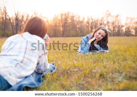Two young women lie on the grass and shooting photos at sunset. Best friends