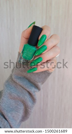 Female hand with long nails and a bottle of emerald green nail polish