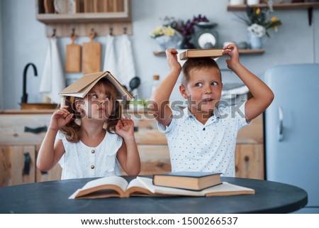 Portrait of two kids with books that sits by the table on the kitchen.