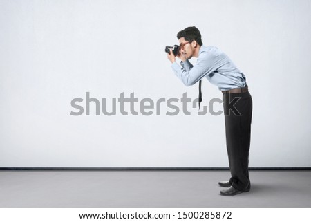 Asian businessman take a picture with his camera over white wall background
