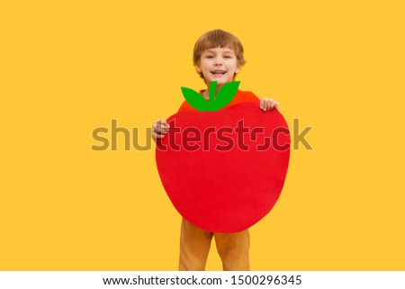 Funny kid with apple from a cardboard on a yellow background. healthy food. Concept summer lifestyle.