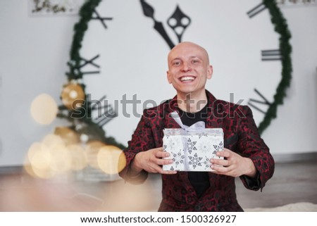 Just smiling and having some fun. Man with big clock behind him sitting with New year gift boxes in holiday clothings.