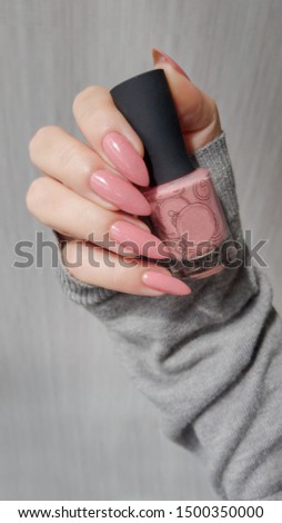 Female hand with long nails and pink manicure holding a bottle of nail polish.