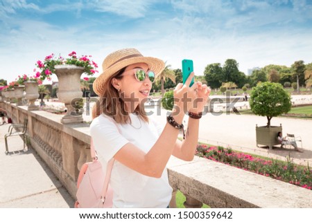 Young asian looking blogger taking pictures on smartphone for social networks of the urban landscape in the Luxembourg garden in Paris. Millennial Travel and lifestyle concept
