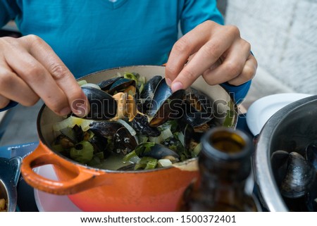Horizontal view of hands of a woman eating traditional mussel and french fries dish called "Moules et Frites"