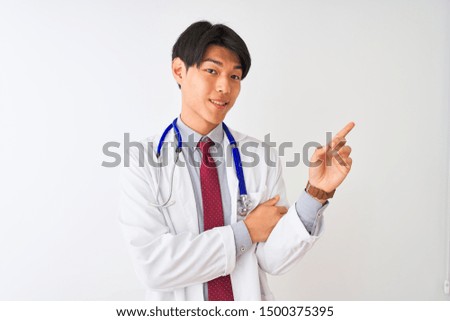 Chinese doctor man wearing coat tie and stethoscope over isolated white background with a big smile on face, pointing with hand and finger to the side looking at the camera.