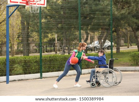 Preteen boy in wheelchair and young woman playing basketball on sports ground