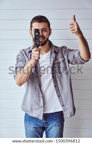 Young emotional man while shooting with old camera on light background