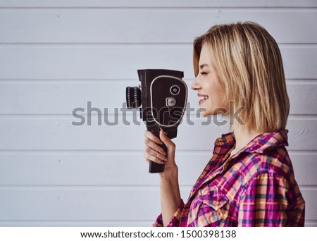 Young emotional girl while shooting with old camera on light background