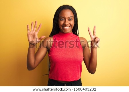 African american woman wearing red casual t-shirt standing over isolated yellow background showing and pointing up with fingers number seven while smiling confident and happy.