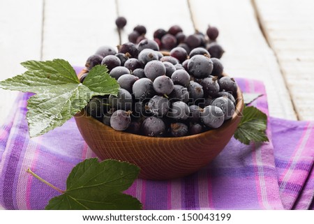 Frozen blackcurrants in wooden bowl on white wooden table. Selective focus.