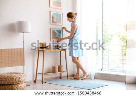 Female interior designer decorating white wall with pictures indoors Royalty-Free Stock Photo #1500458468